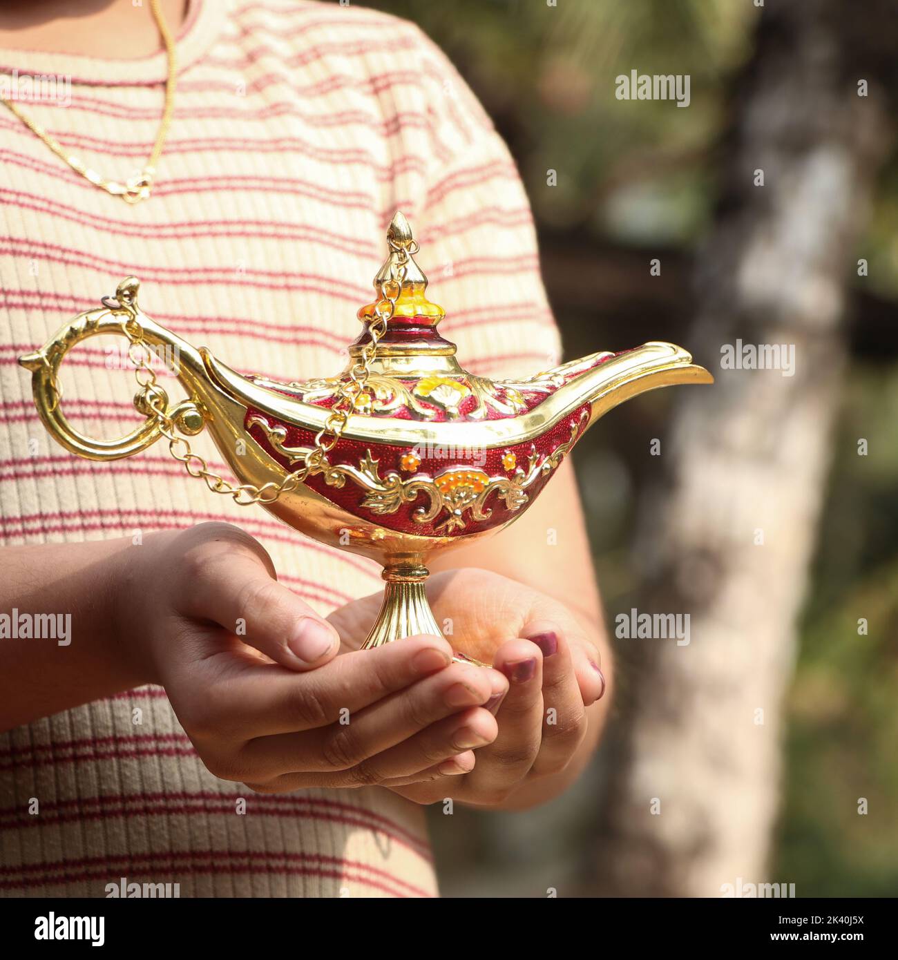 Eine goldene magische Lampe soll einen Genie in den Handflächen eines Kindes in Fantasien halten Stockfoto