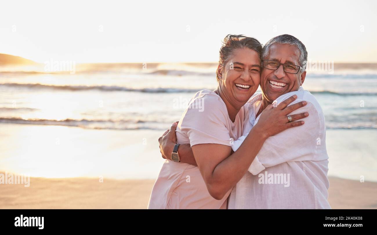 Seniorenpaar, Strandreise und Umarmung am Wasser von Dubai, glücklich im Urlaub für den Ruhestand und Liebe am Meer. Porträt eines älteren afrikanischen Mannes und einer älteren Frau Stockfoto