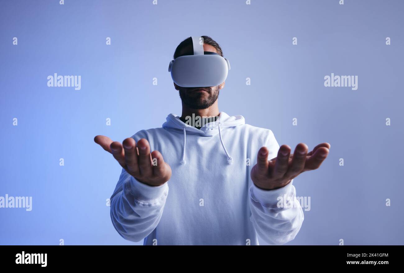 Ein junger Mann hält sich die Hände, während er ein Virtual-Reality-Headset trägt. Junger Mann, der im Studio mit dem virtuellen Raum interagiert. Mann erlebt eine 3D-Simulation Stockfoto