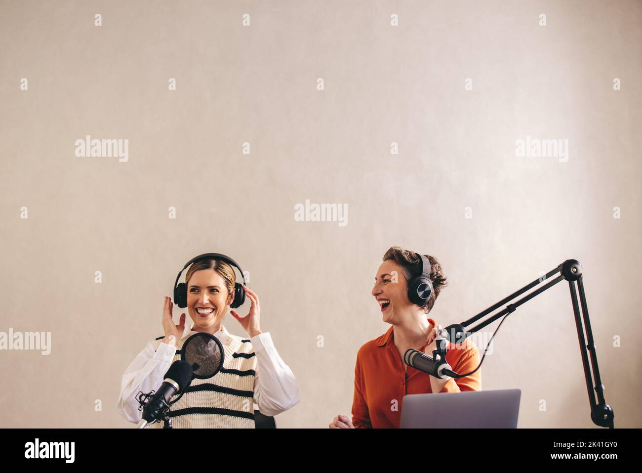 Weibliche Radiomoderatoren lachen und haben eine gute Zeit, während sie eine Live-Audio-Übertragung mithosten. Zwei glückliche Frauen, die eine Live-Podcast-Show auf tei Stockfoto