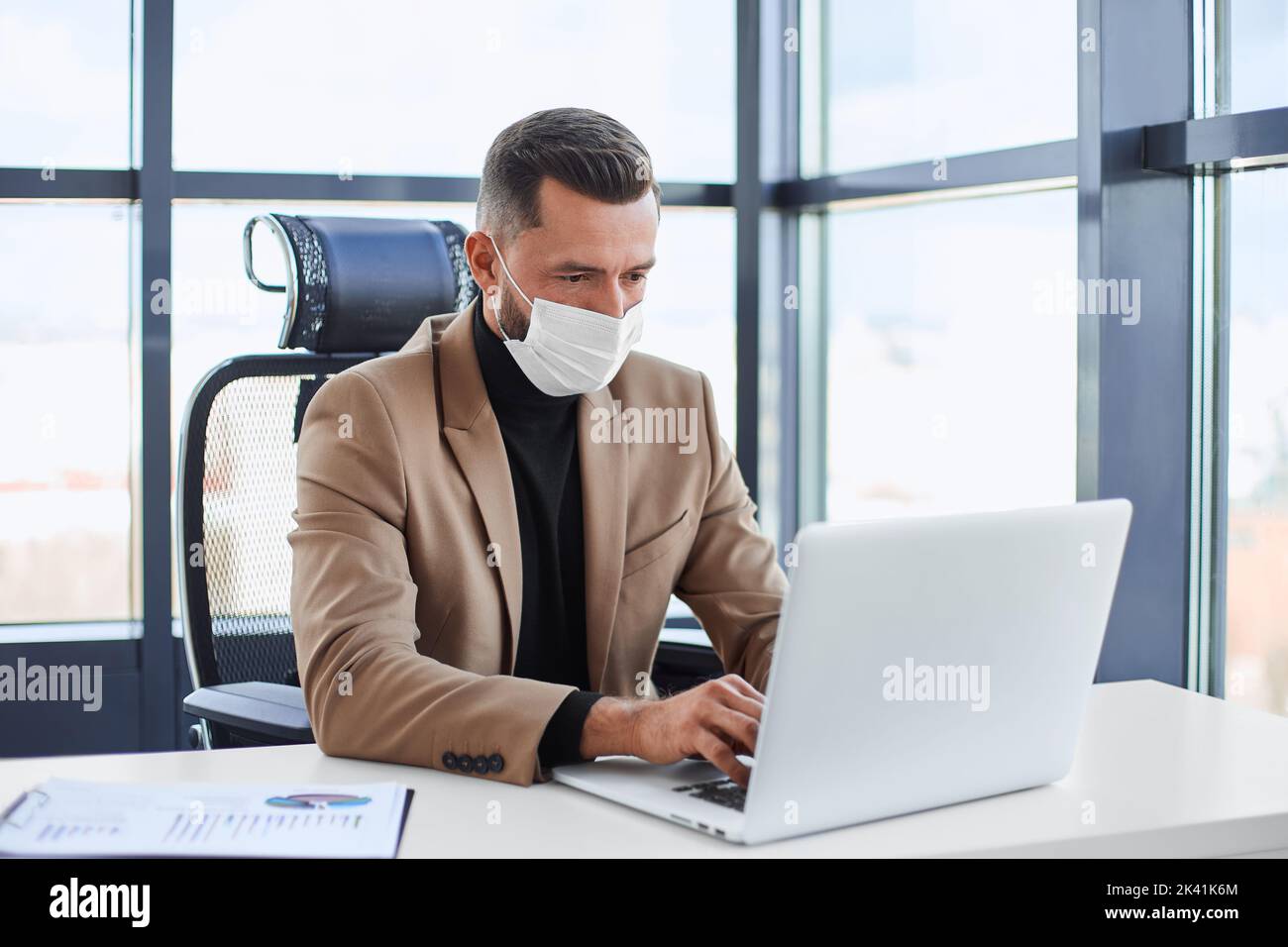 Geschäftsmann in einer Schutzmaske, die an einem Laptop arbeitet. Stockfoto