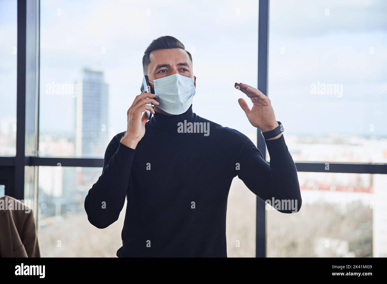 Geschäftsmann in einer Schutzmaske kommunizieren auf einem Smartphone. Stockfoto