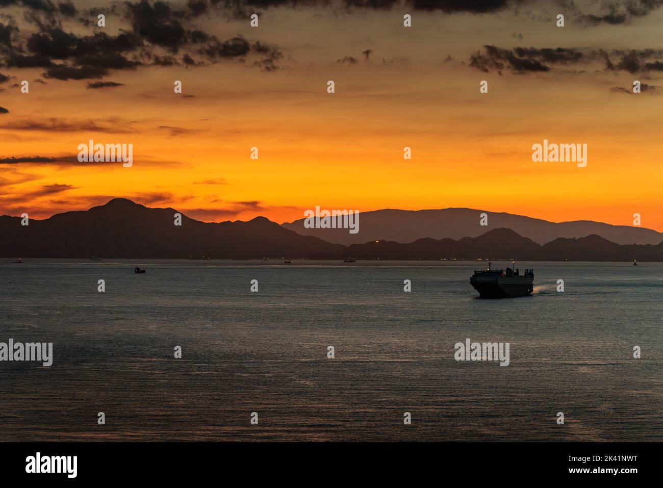 Bei Sonnenuntergang segelt ein kleines Frachtschiff vor der Küste Stockfoto