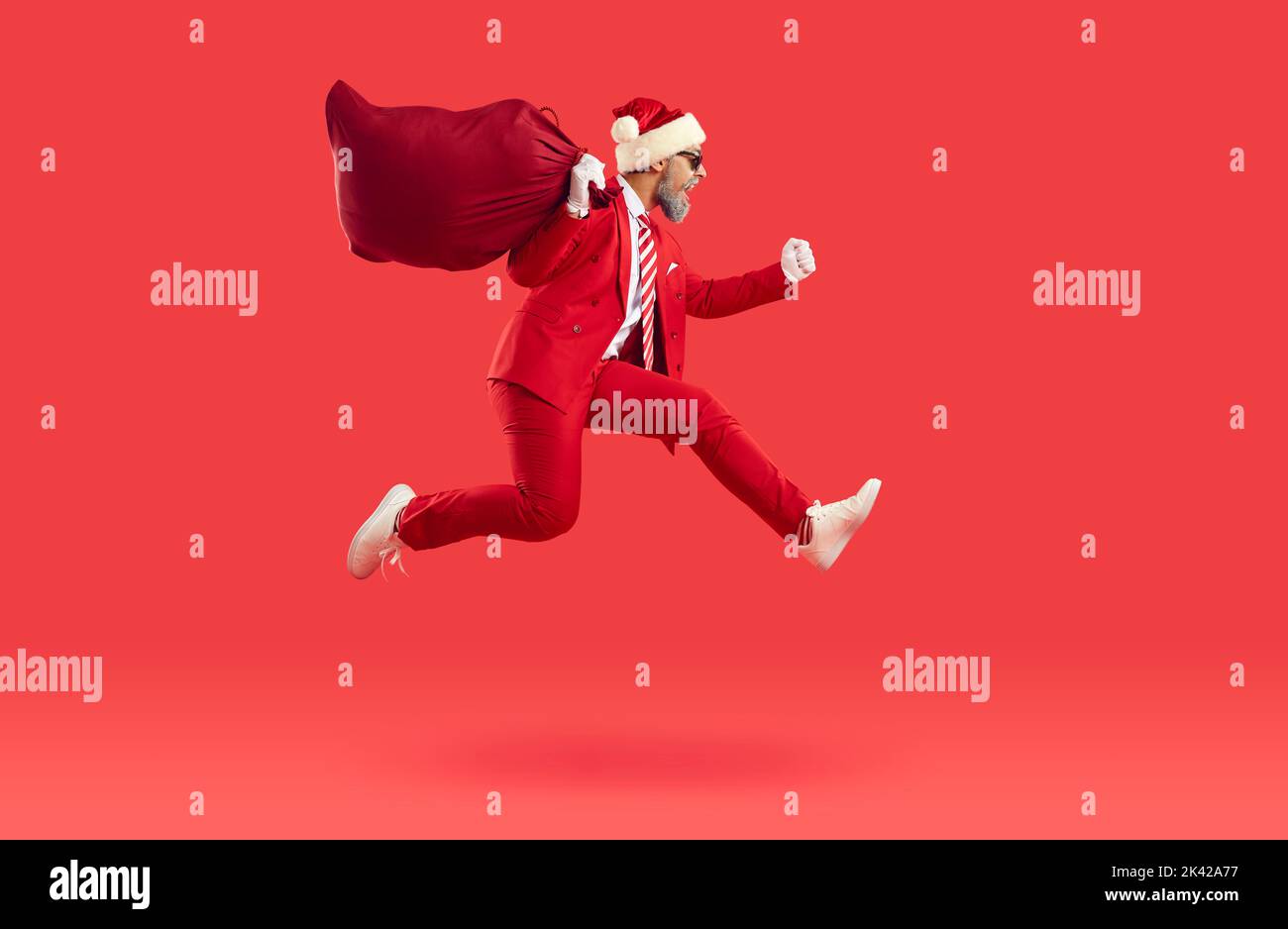 Der Weihnachtsmann in rotem Anzug und Hut liefert Geschenke, trägt einen großen Sack und läuft schnell Stockfoto