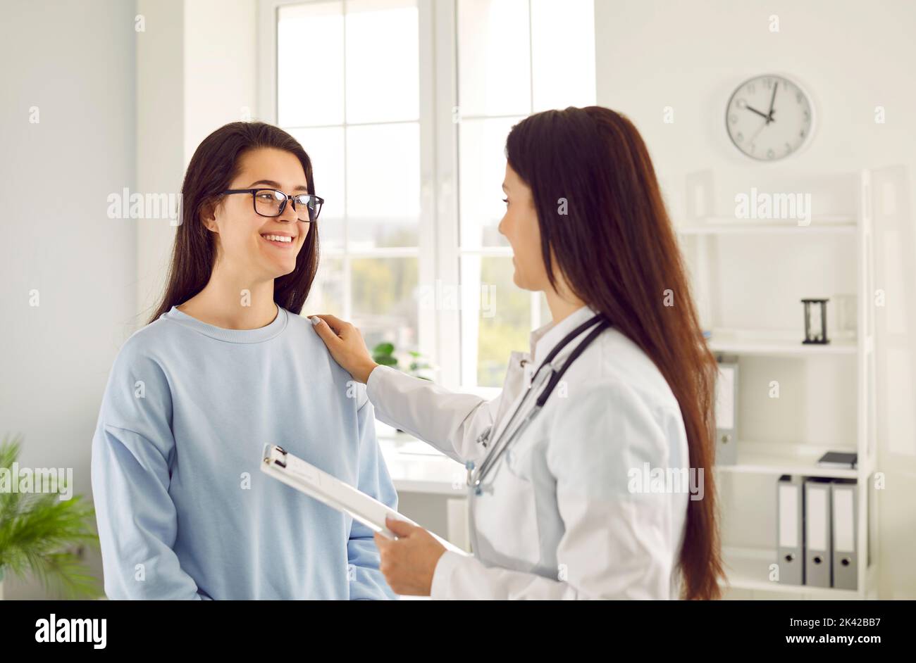Die freundliche Ärztin, die ihre Hand auf die Schulter legt, unterstützt die Patientin durch die Meldung guter Testergebnisse Stockfoto