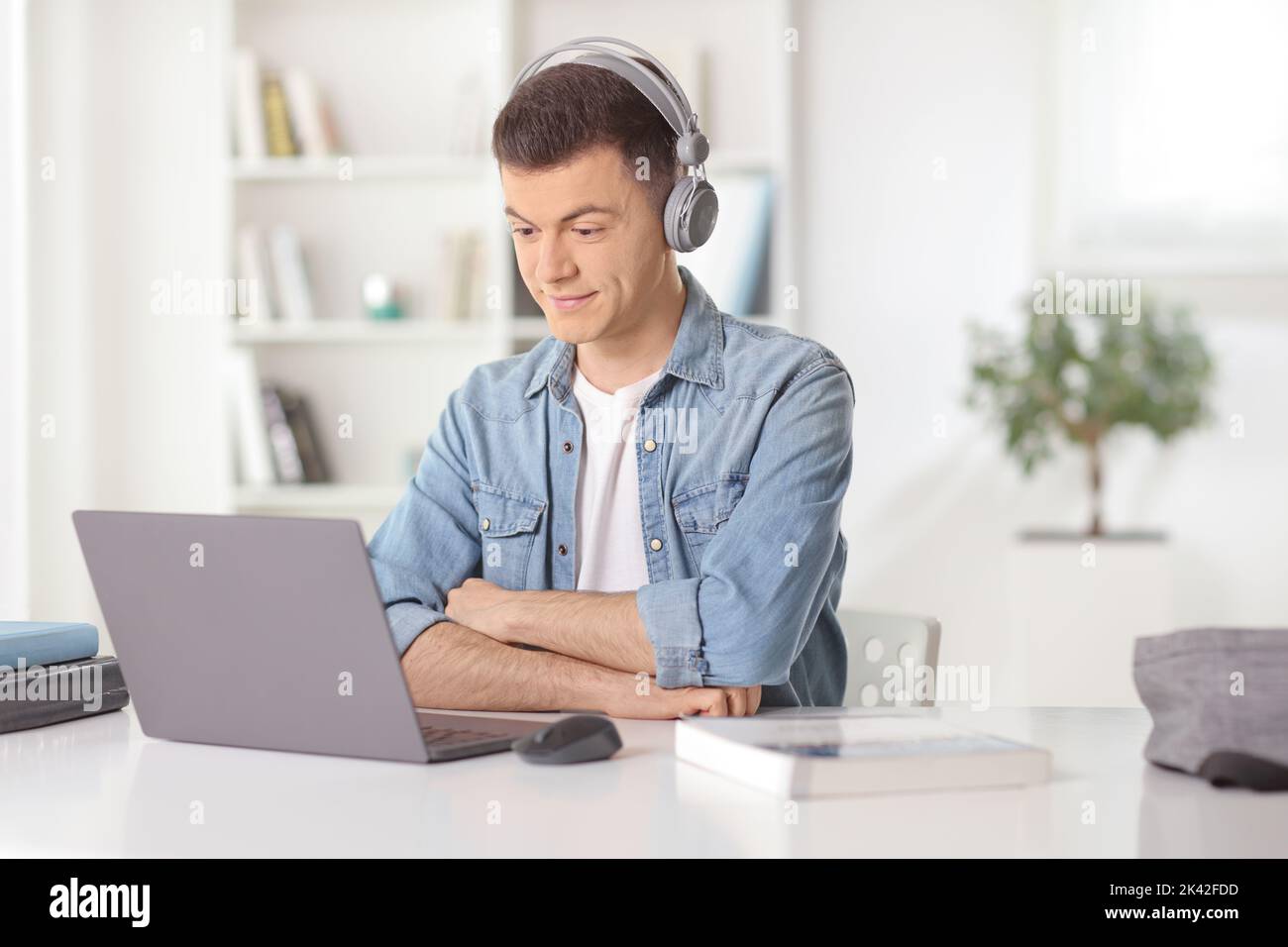 Junger Mann sitzt zu Hause vor einem Laptop und hört sich eine Anleitung mit Kopfhörern an Stockfoto