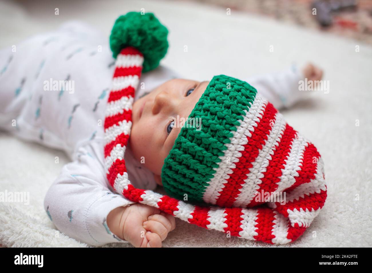 Kleines Baby in gestricktem roten weißen Hut auf roter Decke Stockfoto