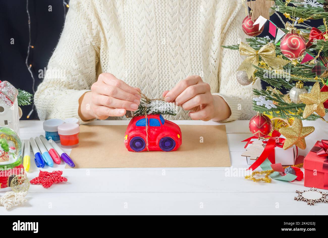 Schritt-für-Schritt Foto-Anleitung für Weihnachten Dekor - ein Mädchen malt eine Gipsmaschine, Schritt 7 - binden Sie einen Weihnachtsbaum auf das Dach Stockfoto
