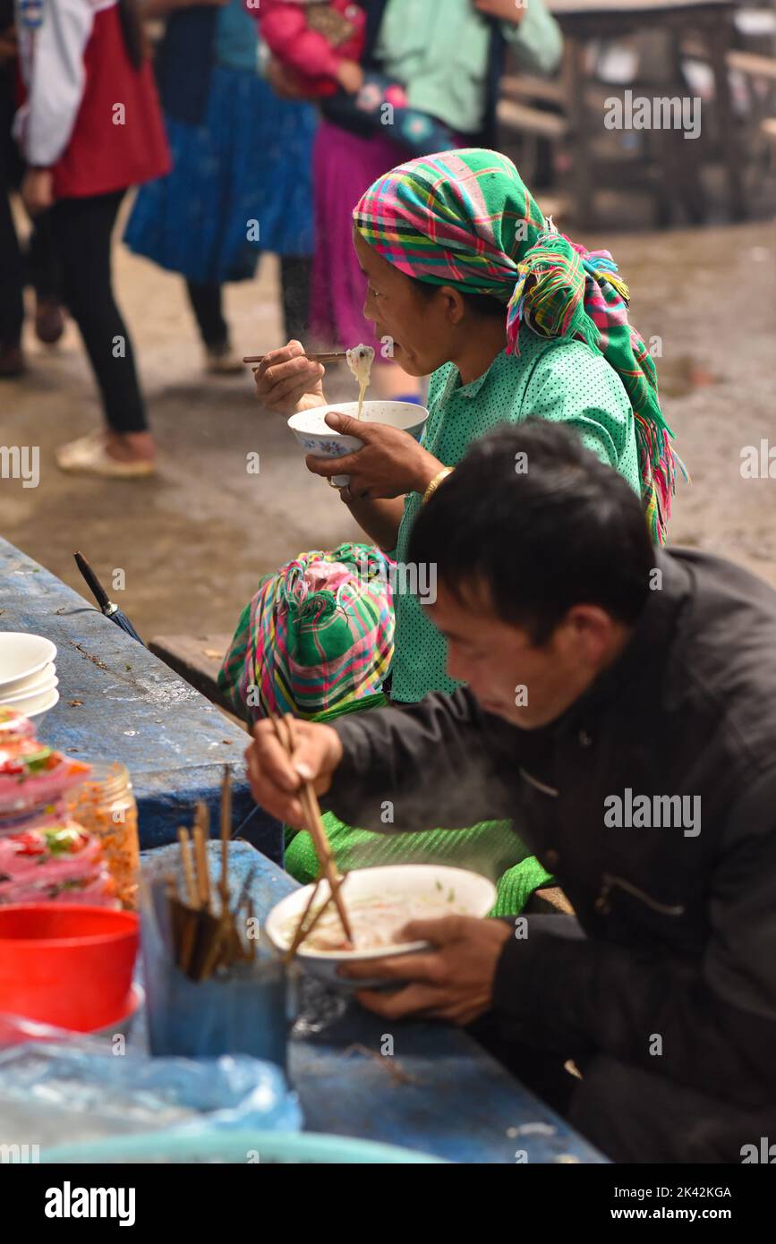 Frau und Mann aus vietnamesischen Volksgruppen tragen traditionelle Kleidung und essen in der Markthalle der Gemeinde Meo Vac, Vietnam. Stockfoto