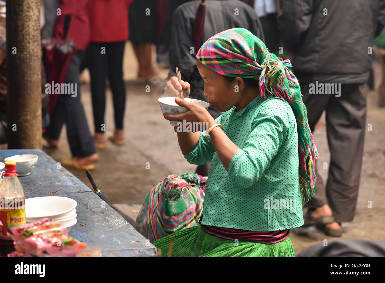 Frau aus einer vietnamesischen ethnischen Gruppe in traditioneller, farbenfroher Kleidung, die in der Markthalle der Gemeinde Meo Vac, Vietnam, zu Mittag gegessen hat. Stockfoto