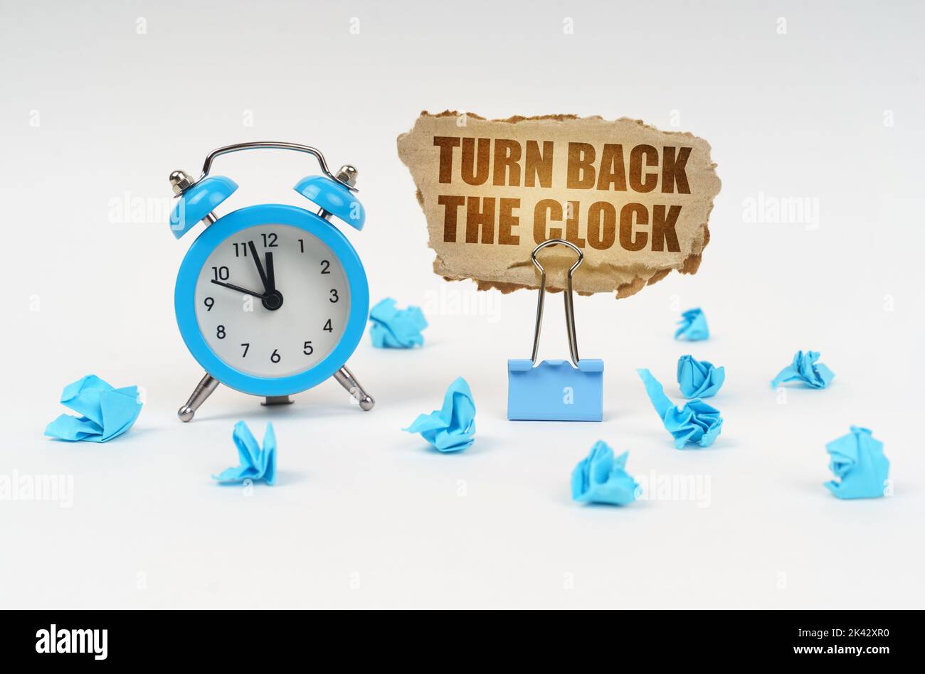 Zeitkonzept. Auf einer weißen Oberfläche, einem Wecker, einem Büroclip, zerknittertem Papier und einem Pappschild mit dem Text - Turn Back The Clock Stockfoto