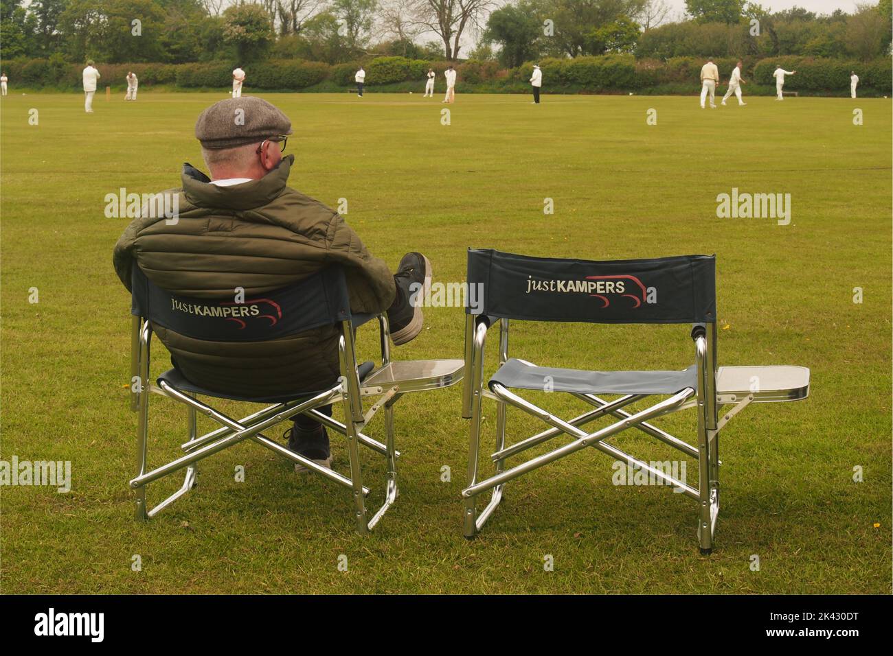 Ein Mann über 60 sitzt auf einem doppelten Campingstuhl, trägt eine flache Kappe und beobachtet ein Cricket-Spiel auf dem Belstone Cricket Ground, Dartmoor, Devon, England Stockfoto