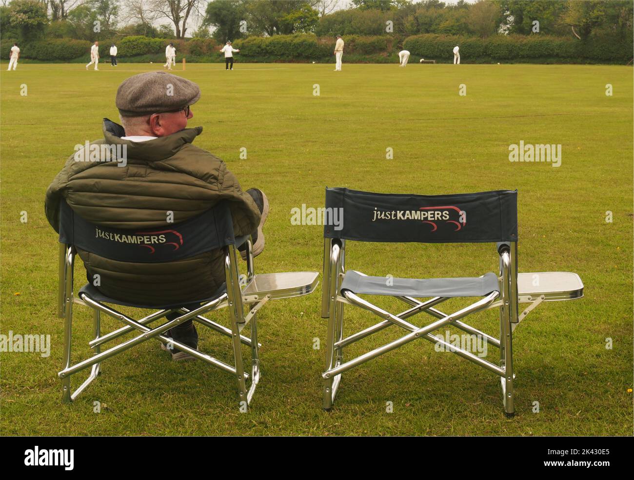 Ein Mann über 60 sitzt auf einem doppelten Campingstuhl, trägt eine flache Kappe und beobachtet ein Cricket-Spiel auf dem Belstone Cricket Ground, Dartmoor, Devon, England Stockfoto