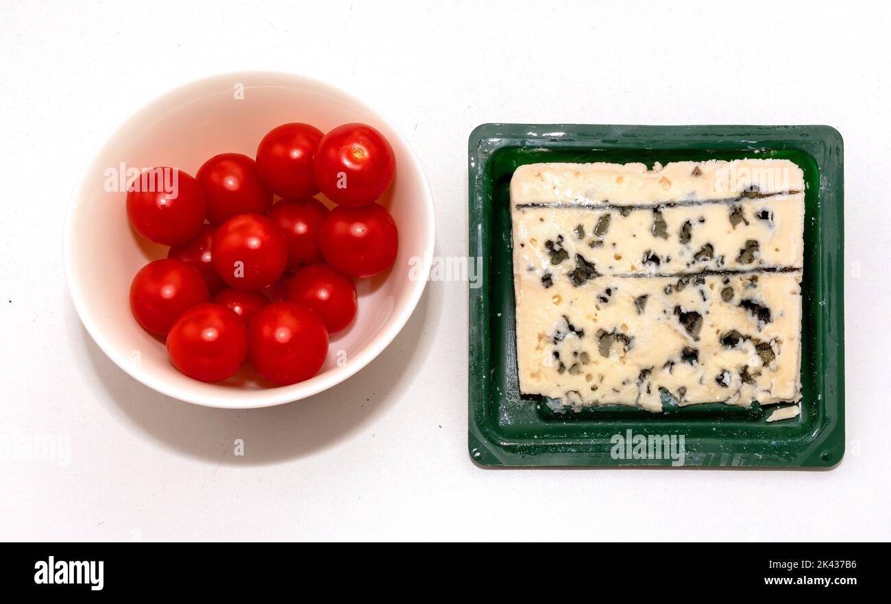 Schimmeliger roquefort-Blauschimmelkäse neben einer Schüssel mit frischen Bio-Pflaumentomaten Stockfoto
