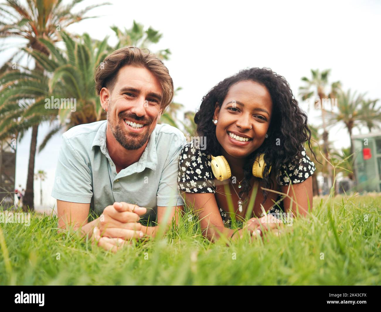 Lächelndes junges, multiethnisches heterosexuelles Paar, das auf dem Gras in einem Park liegt Stockfoto