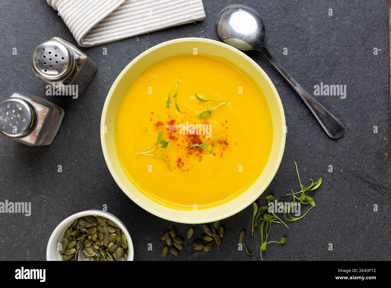 Horizontale Abbildung einer Schüssel Karottensuppe mit Garnierung, Gewürzen, Löffel und Kürbiskernen auf Schiefer Stockfoto