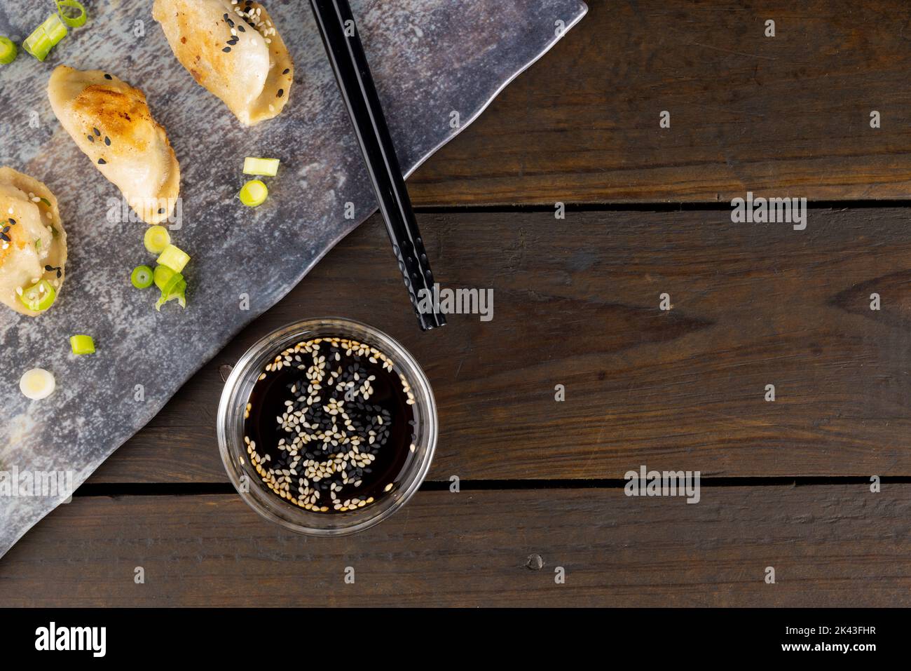 Blick von oben auf asiatische Knödel, Sojasauce und Essstäbchen mit Schiefer und Holzhintergrund Stockfoto