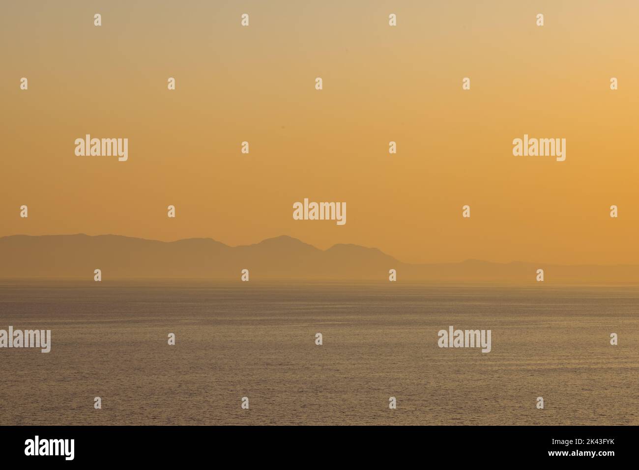 Meereslandschaft, Seeufer mit Bergen, wolkenloser Himmel bei Sonnenuntergang und Horizont Stockfoto