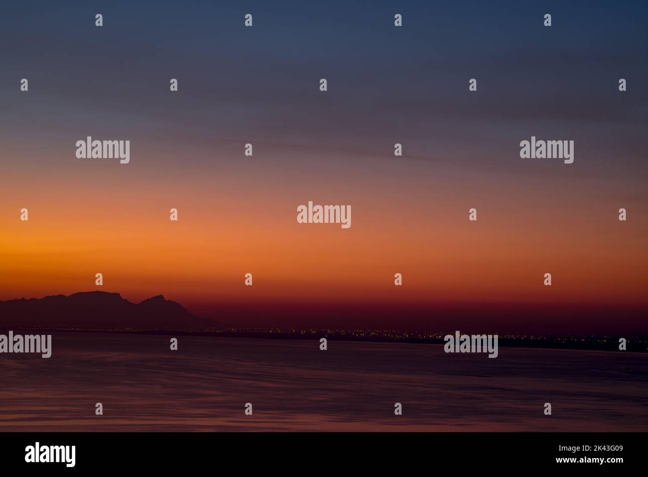 Meereslandschaft, Seeufer mit Bergen, wolkenloser Himmel bei Sonnenuntergang und Horizont Stockfoto