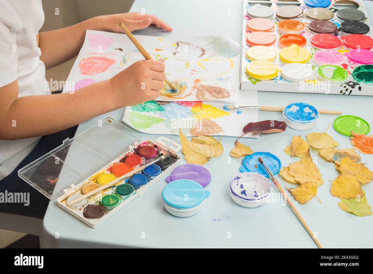 Kind malt und zeichnet mit Aquarellen und Fingerfarben. Drucken von Blättern auf Papier. Kinder spielen, erziehen in der bildenden Kunst. Kinder Kreativität. Stockfoto