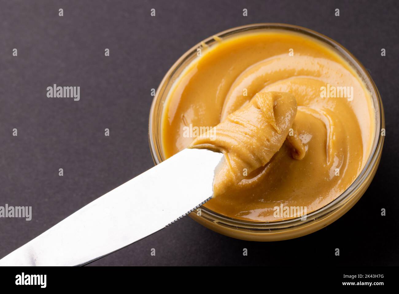 Bild von Messer und Schüssel mit Erdnussbutter auf dunkelgrauem Hintergrund Stockfoto