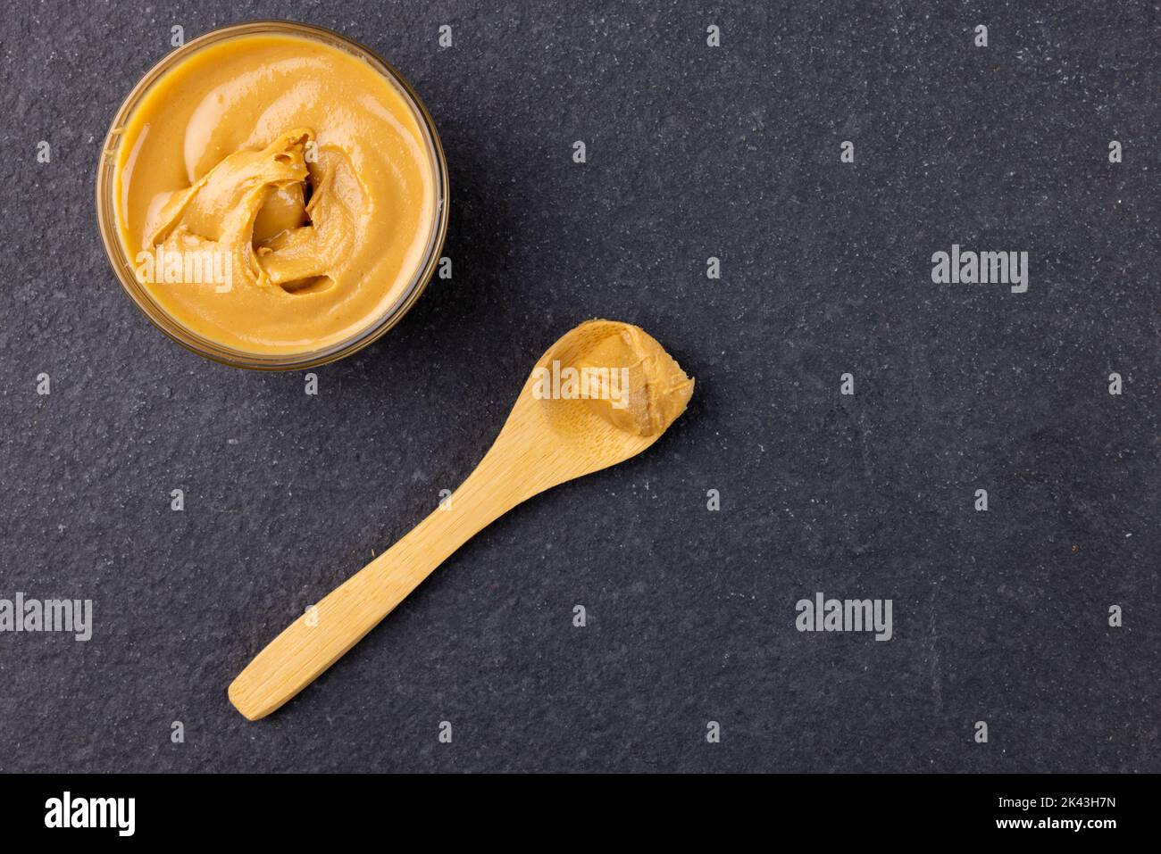 Bild von Löffel und Schüssel mit Erdnussbutter auf dunkelgrauer Oberfläche Stockfoto