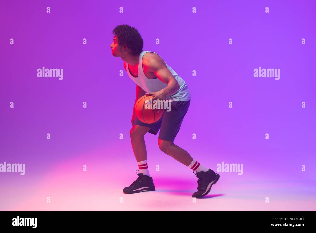 Bild von biracial Basketballspieler mit Basketball auf neon-lila Hintergrund Stockfoto