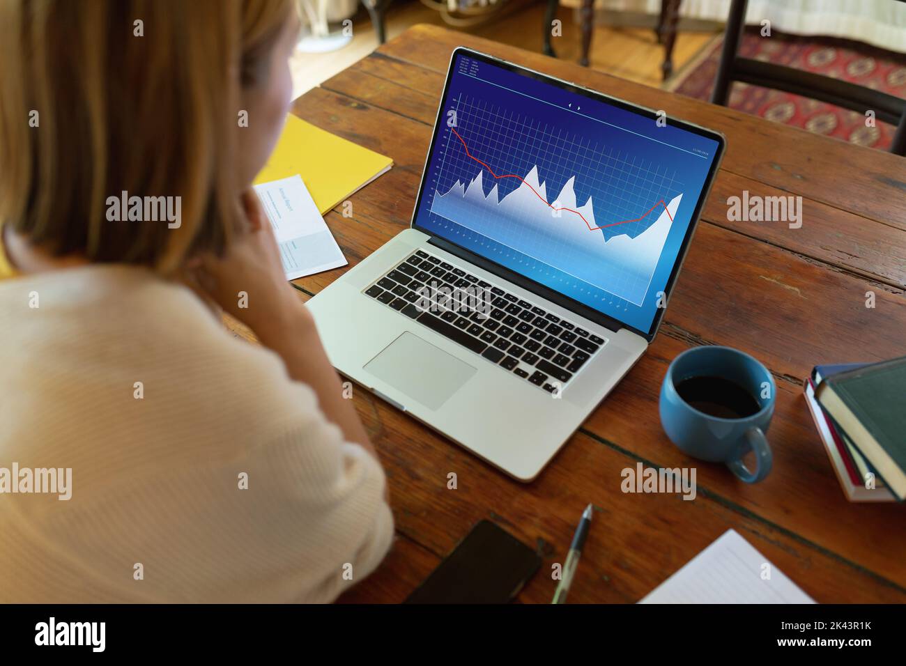 Blonde asiatische Geschäftsfrau analysiert Diagramme über Laptop auf Schreibtisch im Büro Stockfoto