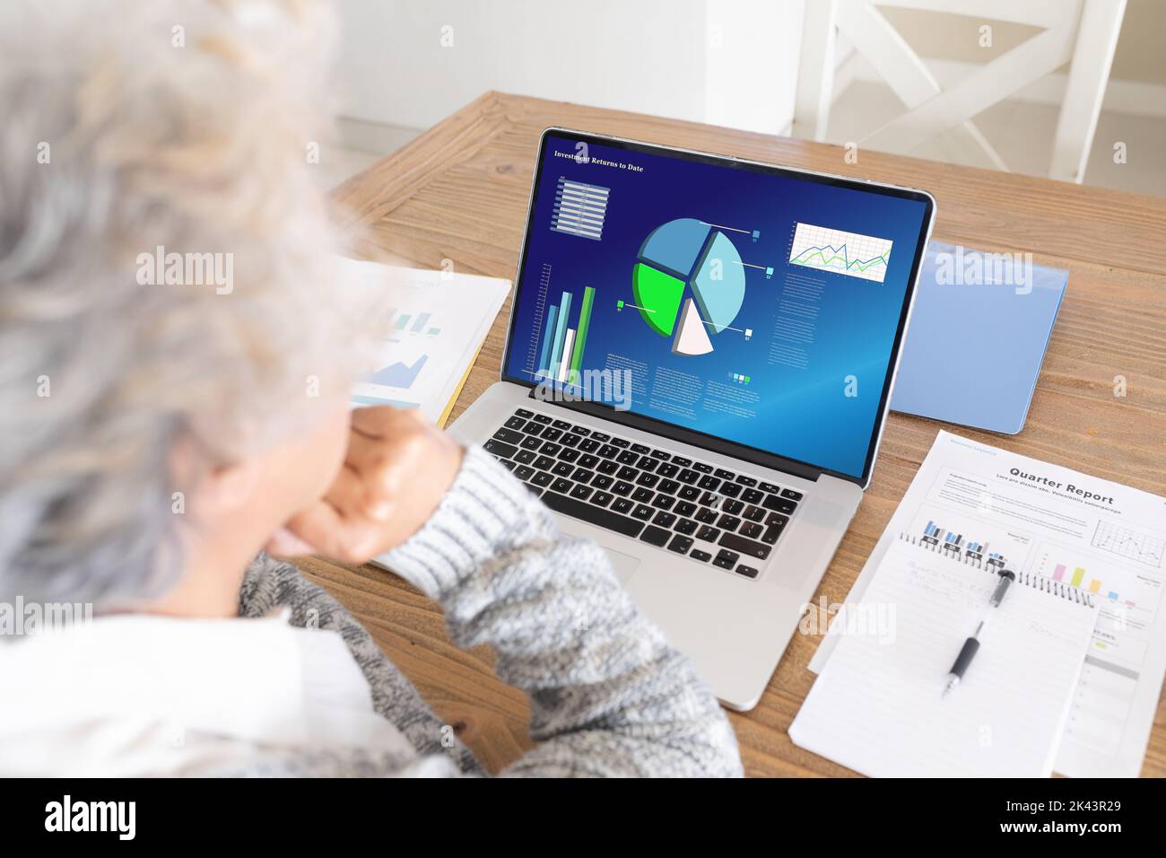 Eine ältere kaukasische Frau, die Geschäftsdiagramme über einem Laptop auf dem Schreibtisch im Firmenbüro analysiert Stockfoto