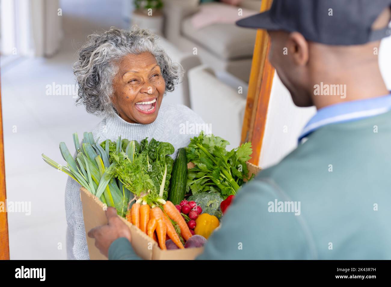 Glückliche ältere afroamerikanische Frauen erhalten eine Schachtel mit Gemüse vom Lieferanten Stockfoto