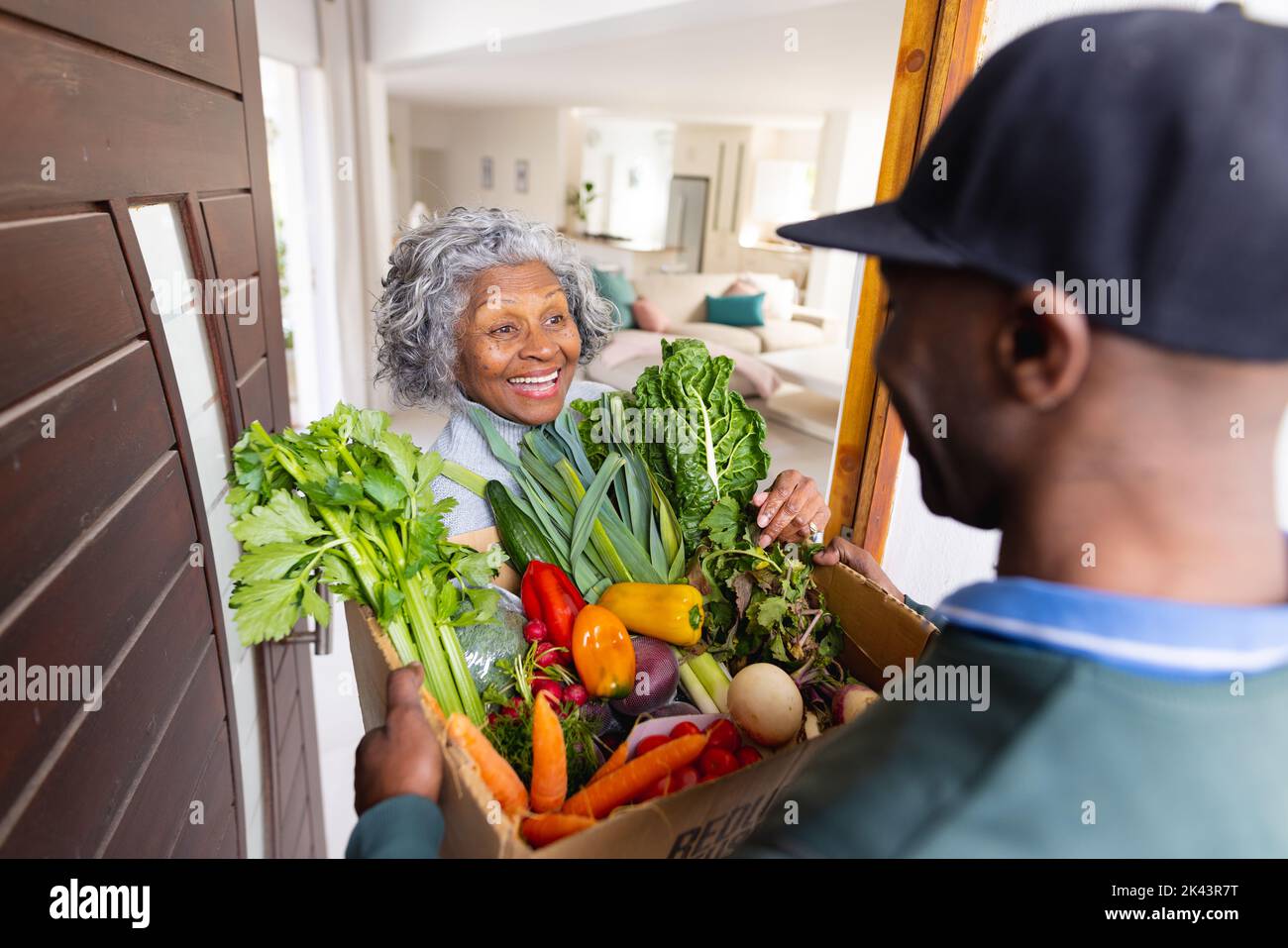 Glückliche ältere afroamerikanische Frauen erhalten eine Schachtel mit Gemüse vom Lieferanten Stockfoto