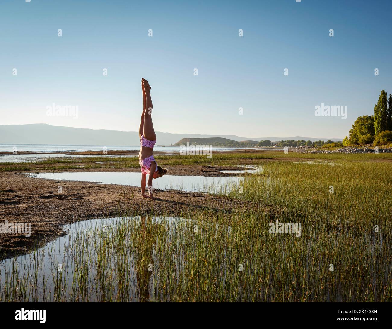 Teenager (14-15) im Bikini, die bei Sonnenaufgang Handstand am See aufführt Stockfoto