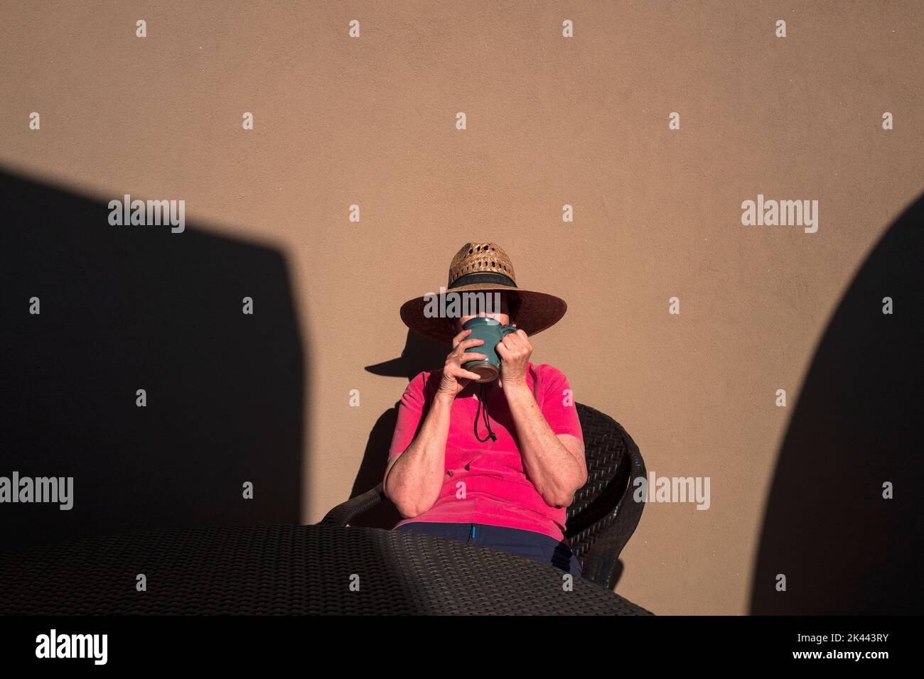 Eine Frau, die Kaffee an der wand von lehmziegeln trinkt, auf einer sonnenbeleuchteten Terrasse Stockfoto