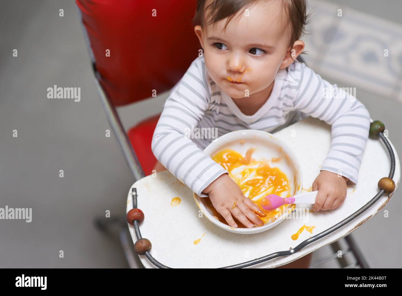 Ich bin immer noch ein bisschen peckish. Ein nettes kleines Baby sitzt in einem Hochstuhl essen. Stockfoto