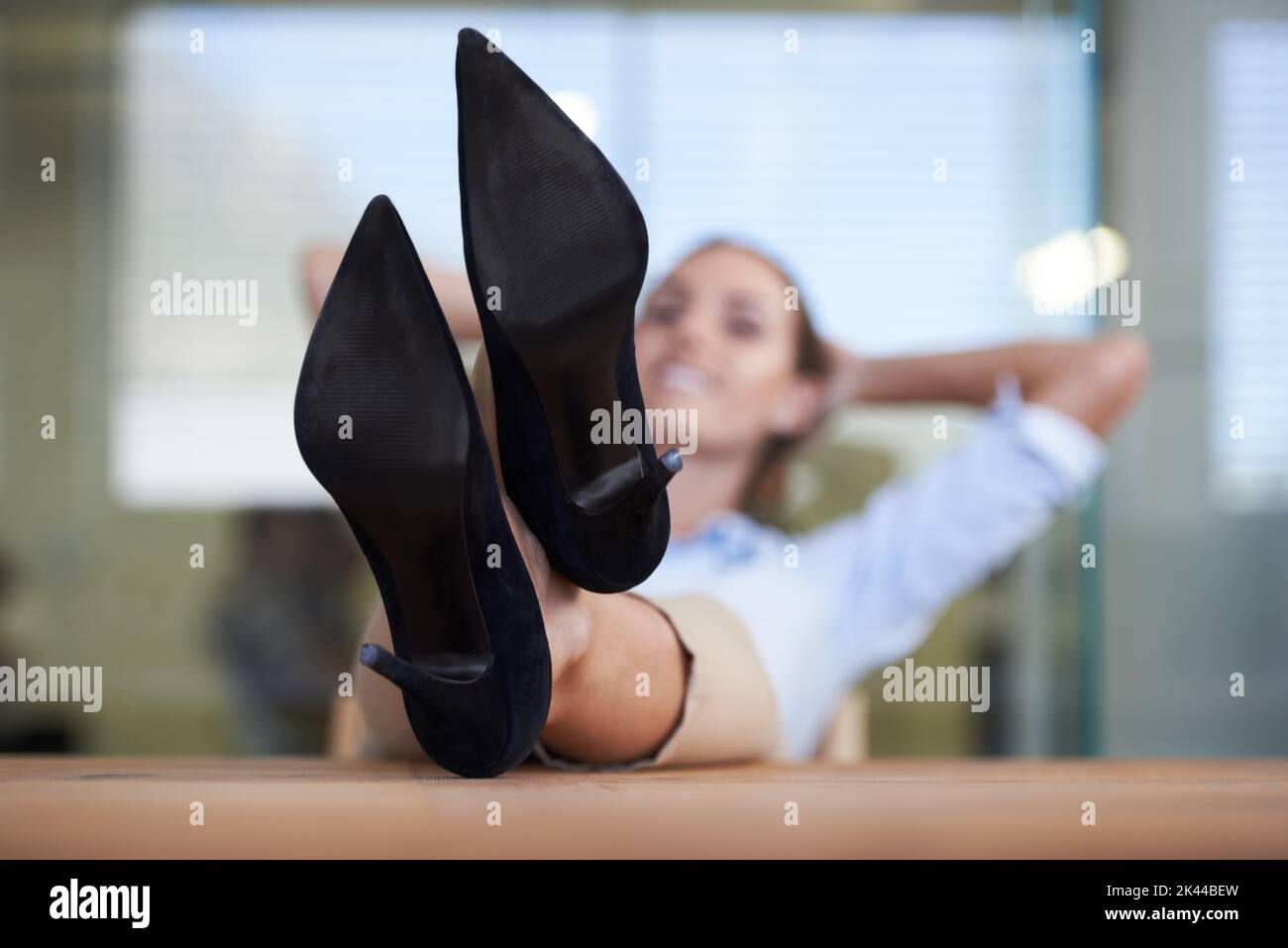 Heres to a Job Gut gemacht. Eine Geschäftsfrau, die sich mit den Füßen auf ihrem Schreibtisch zurücklehnen kann. Stockfoto