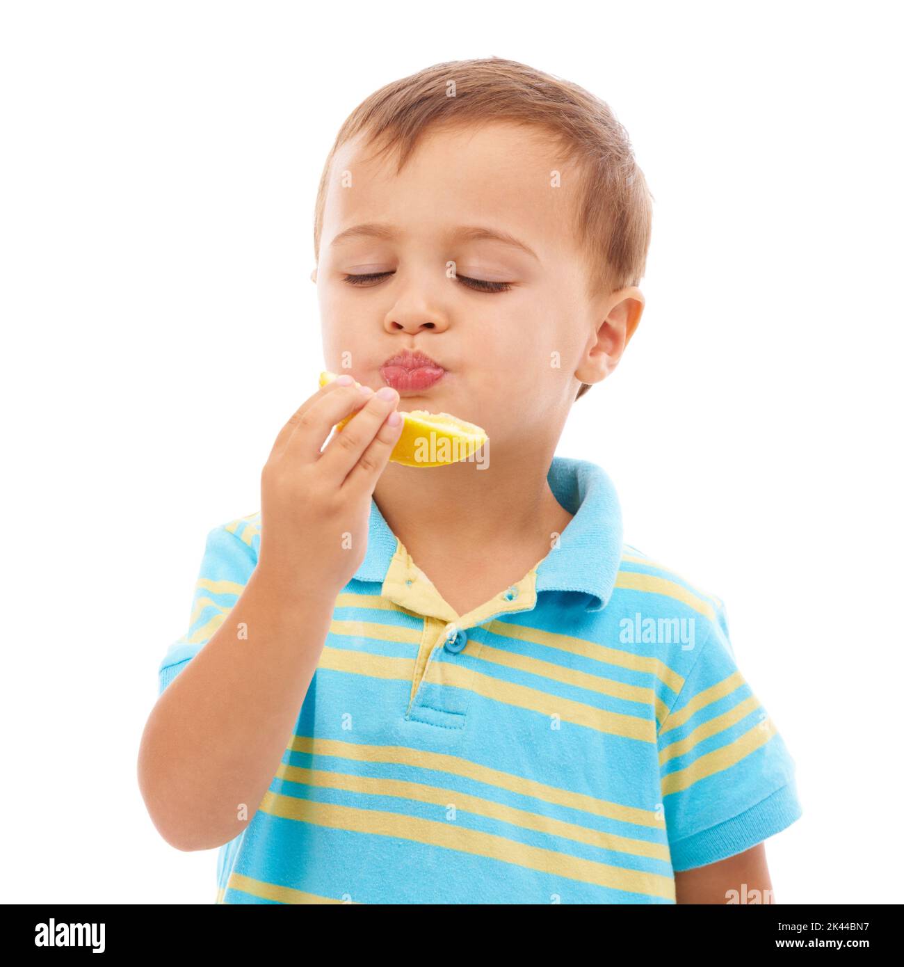 Ein süßer Junge, der eine orangefarbene Scheibe auf Weiß isst. Stockfoto