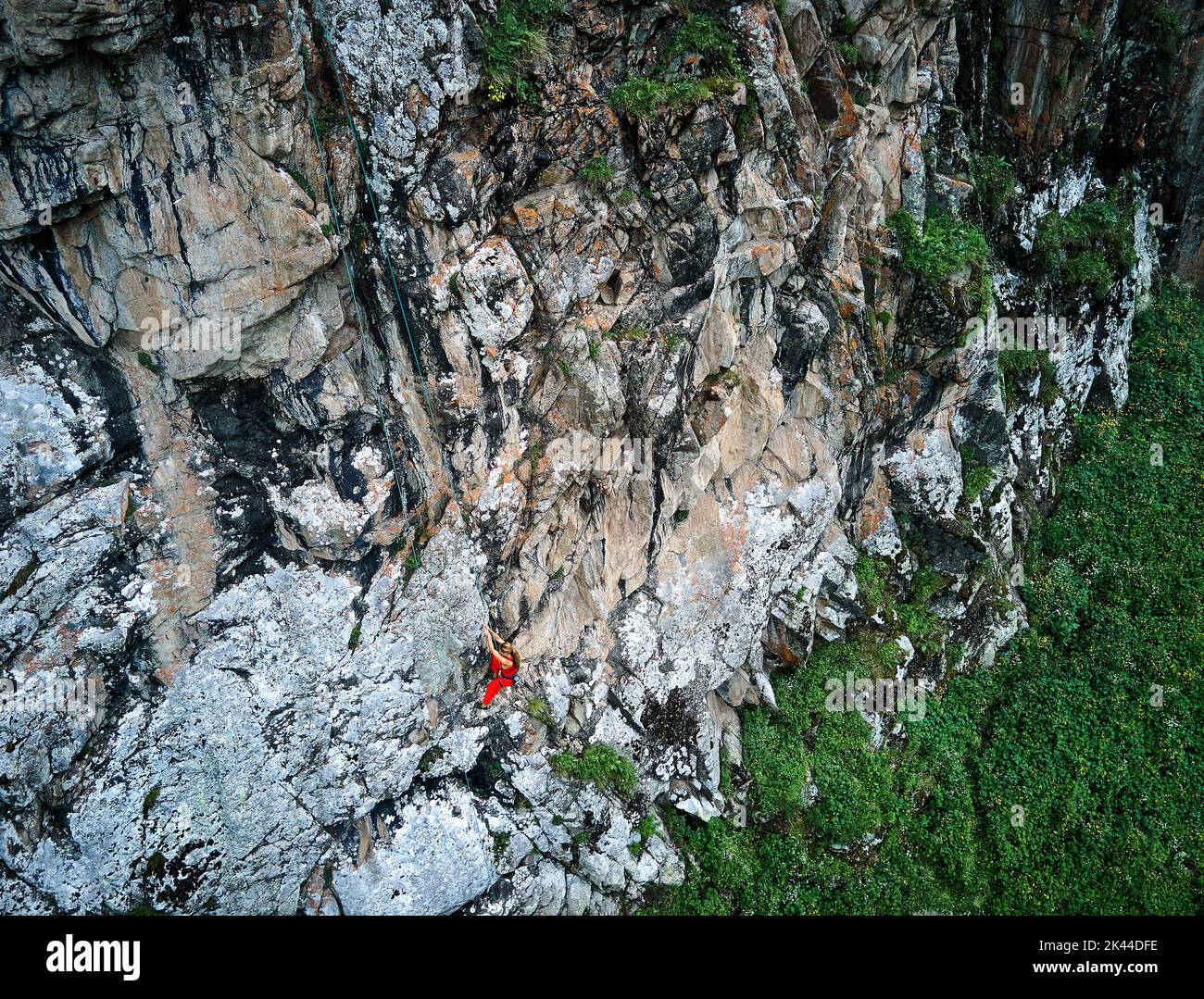 Drohnenaufnahme einer starken Frau im roten Hemd, die auf dem hohen Felsen in den Bergen Tyan Shan in Kasachstan klettert Stockfoto