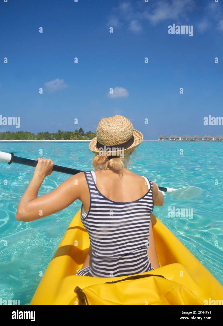 Paddeln ins Paradies. Eine schöne junge Frau, die auf einem Boot in einem tropischen Ozean paddelt. Stockfoto