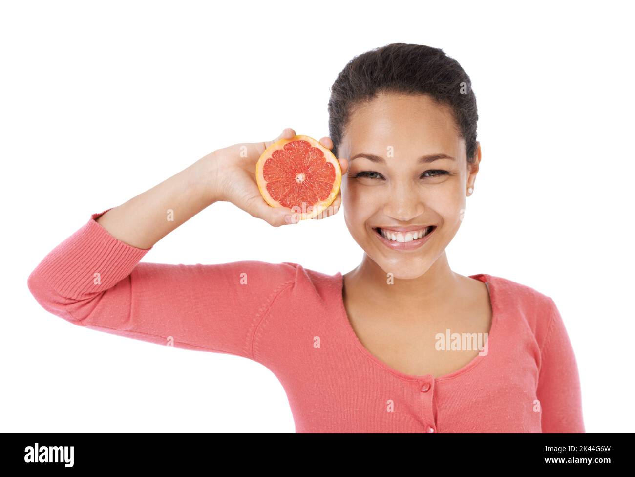 Es ist reich an Antioxidantien. Junge Frau lächelt, während sie eine Grapefruit hochhält - isoliert auf Weiß. Stockfoto