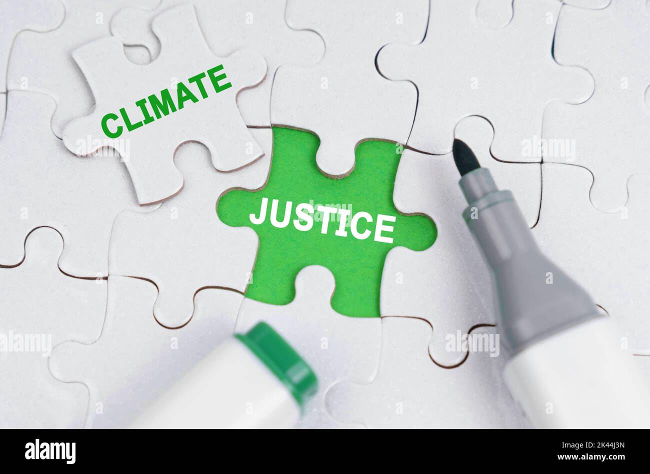 Ökologisches Konzept. Weiße Rätsel liegen auf einem grünen Hintergrund, anstelle eines offenen Puzzles steht geschrieben - Climate Justice Stockfoto