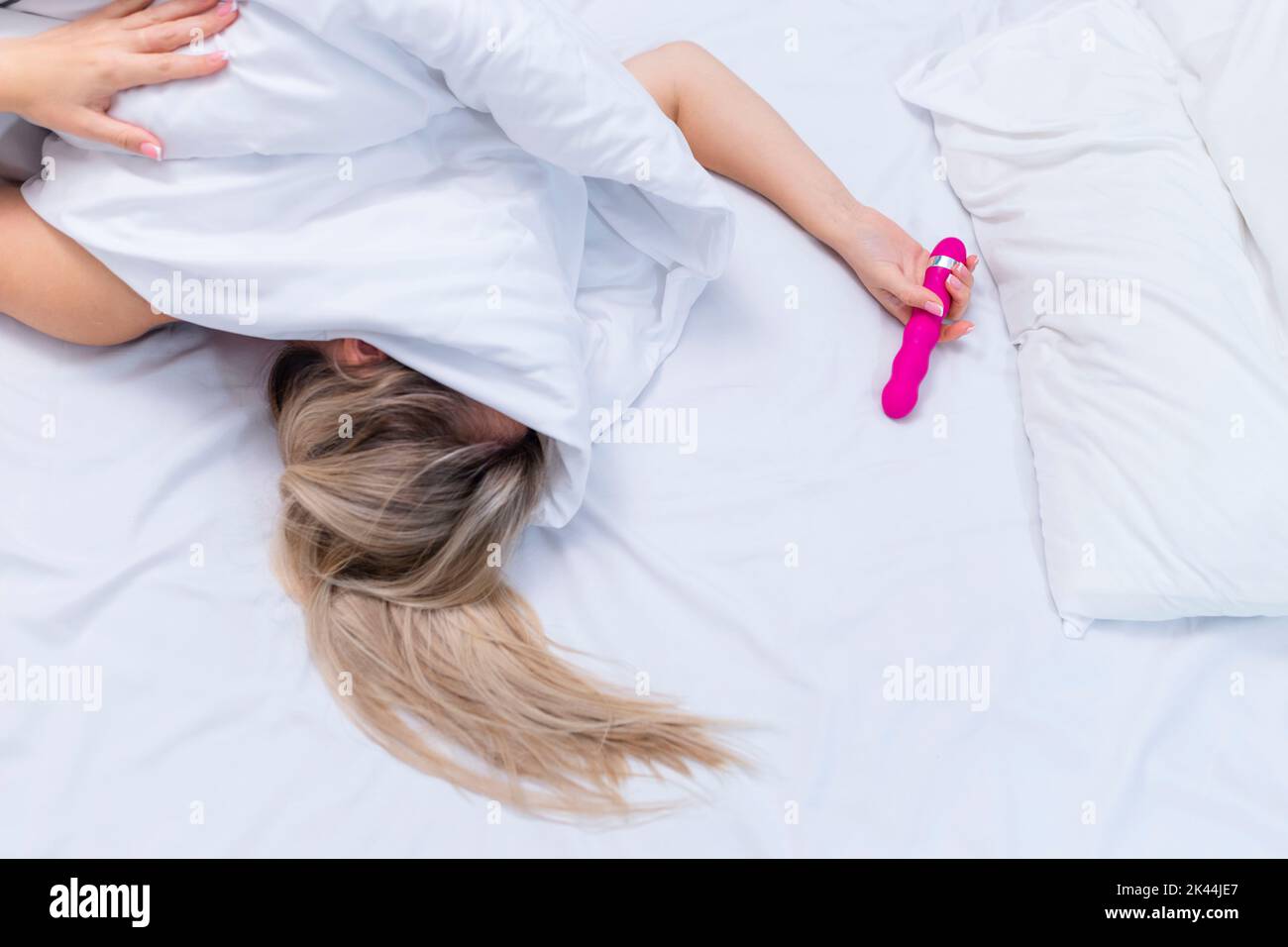 Frau im Bett unter den Laken, die den Vibrator in der Hand hält Stockfoto