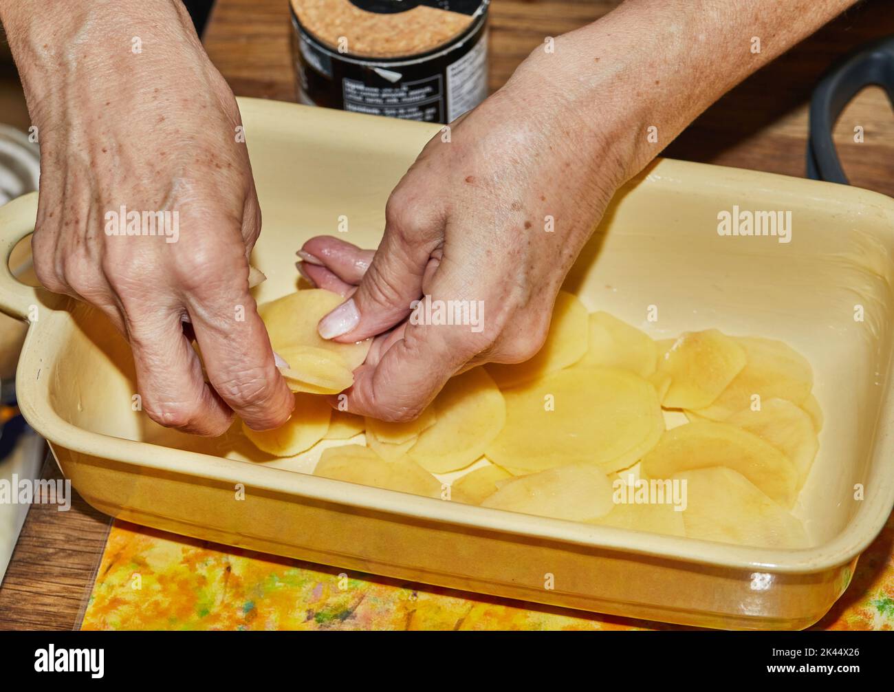 Schritt-für-Schritt-Rezept für Kartoffelgratin. Die Hände stapeln Kartoffelscheiben in eine Glasbackform. Kartoffelauflauf Stockfoto