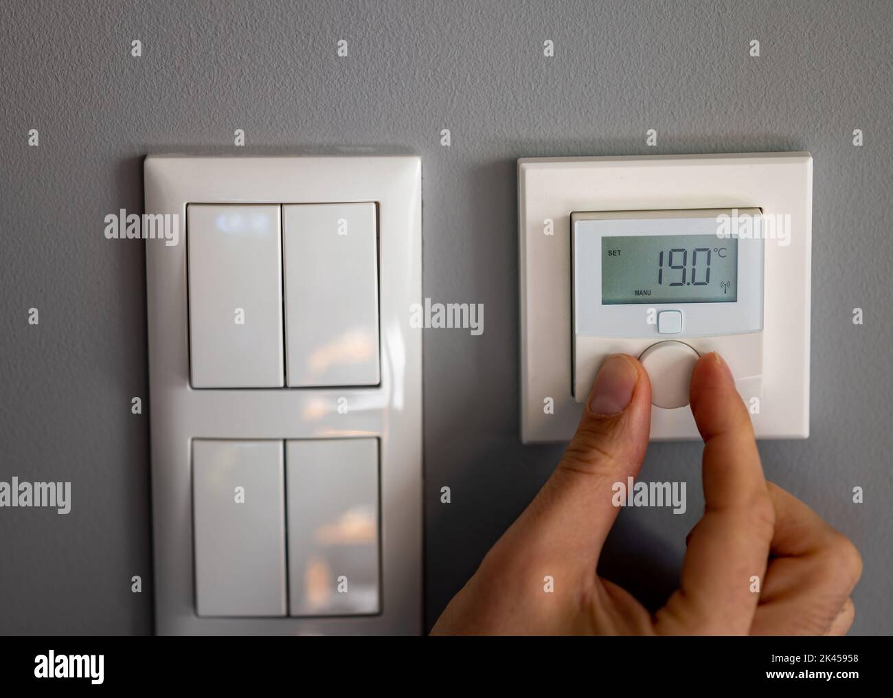 Hand dreht die Temperatur auf 19 Grad Celsius auf einem elektronischen Thermostat. Symbol für Energieeinsparung. Stockfoto