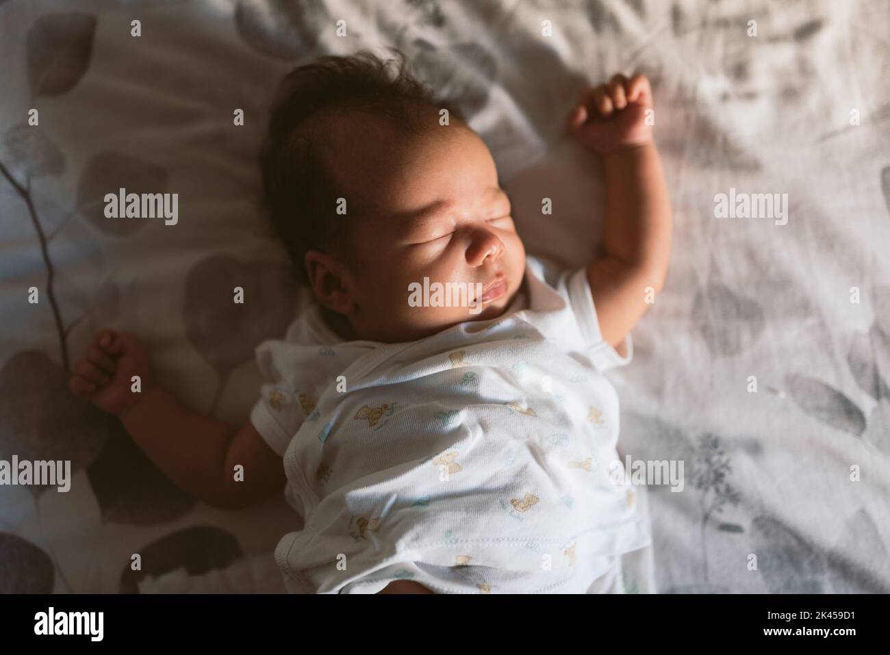 2 Monate altes neugeborenes Baby, das morgens friedlich im Bett schläft, mit natürlichem Licht und weißem Pijama Stockfoto