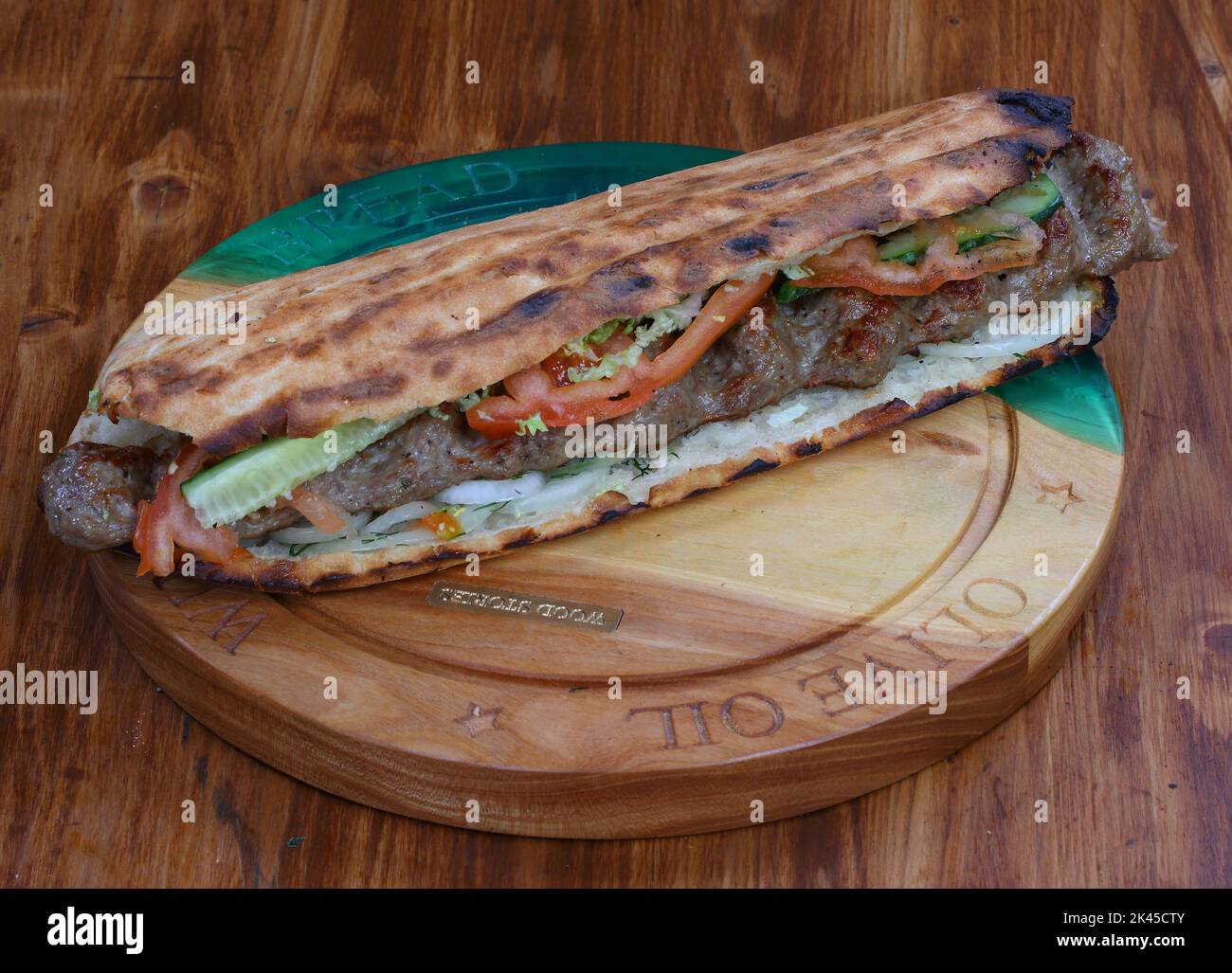 Rolle gefüllt mit Shish Kebab mit Tomaten, Kräutern, Ketchup und Amyonnaise auf einem Holztisch Stockfoto