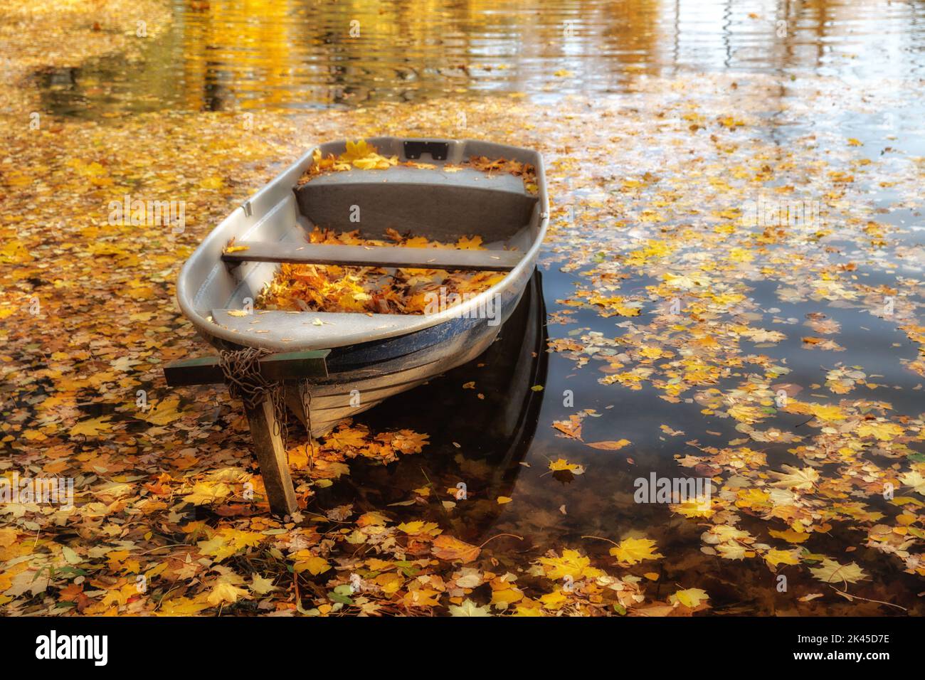 Farbenfrohe Herbstlandschaft. Holzboot auf dem See, übersät mit gefallenen gelben Blättern. Natürlicher, saisonaler Hintergrund Stockfoto