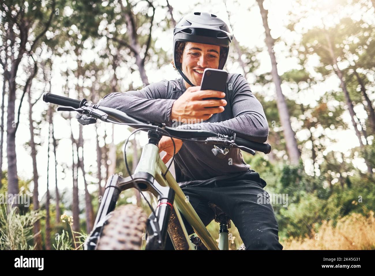 Radfahrer, Telefon und Fahrrad glücklich im Wald auf Fahrt für Fitness, Gesundheit und Wellness. Mann, Smartphone und Fahrrad über Social Media oder App zur Kommunikation Stockfoto
