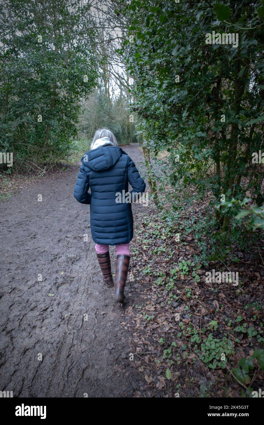 Eine alleinreisende ältere Frau, die auf einem schlammigen Waldweg entlang der Hertfordshore-küste englands läuft Stockfoto