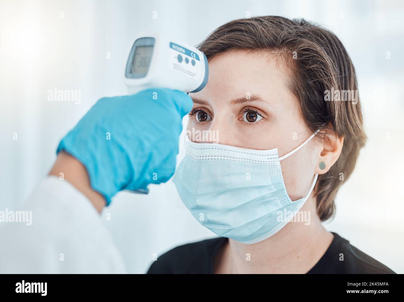 Covid, Thermometer und Arzt scannen die Fiebertemperatur der Frau mit einer Maske, die im Krankenhaus konsultiert wird. Patiententest für Frauen für Gesundheit, Sicherheit und Stockfoto