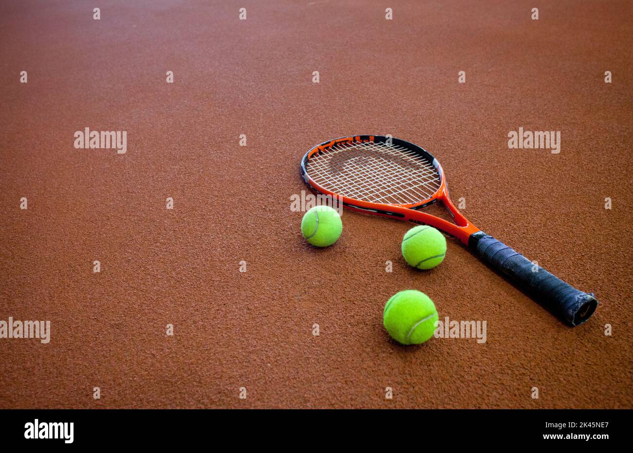 Ein harter Tennisplatz und ein Tennisquet, mit drei Bällen. Stockfoto